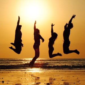 Mentaltraining – Workshops: Silhouetten von vier Menschen, die an einem Strand in die Höhe springen, dahinter die untergehende Sonne